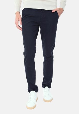 Chino blu navy in cotone, con un taglio slim, una texture sottile e tasche laterali, abbinati a sneakers bianche e un maglione leggero.