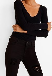 Top negro de manga larga acanalado con escote en V profundo, combinado con jeans skinny negros rasgados, que presentan bordes desgastados en las zonas de las rodillas.