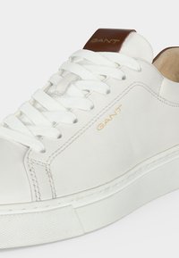 Baskets en cuir blanc avec des lacets blancs, languette en cuir marron au talon, logo doré « GANT » sur le côté et le talon, semelle en caoutchouc blanche.