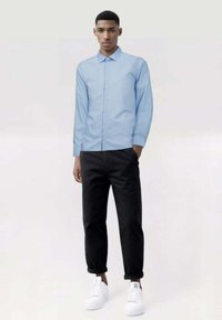 Camisa de manga larga azul claro con cierre de botón, combinada con pantalones negros ajustados y zapatillas blancas. Tela suave con un ajuste casual.