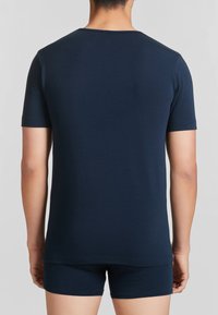 T-shirt blu navy con maniche corte, scollatura rotonda e texture liscia. Indossato con pantaloni corti abbinati. Vista posteriore focalizzata sulla semplicità.