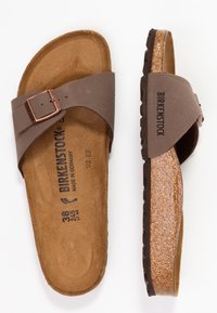 Rjave sandale s korakom iz plute, z enim nastavljivim trakom in bronasto sponko. Teksturirana gumijasta podplat. Notranja oznaka velikosti 38. Oznaka Birkenstock je vidna.