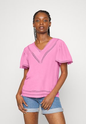 Top rosa em V com mangas curtas e bufantes, apresentando detalhes em renda ao longo do decote e da barra, feito de tecido macio. Combinado com calções de ganga.