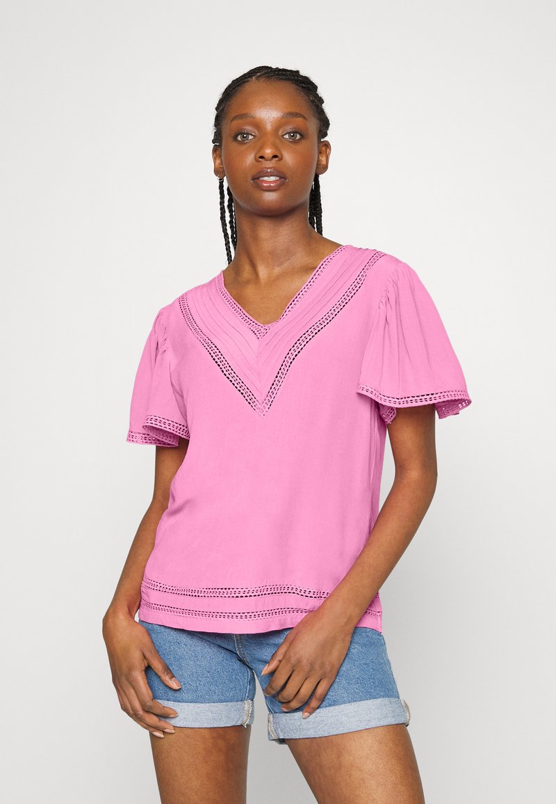Top rosa em V com mangas curtas e bufantes, apresentando detalhes em renda ao longo do decote e da barra, feito de tecido macio. Combinado com calções de ganga.