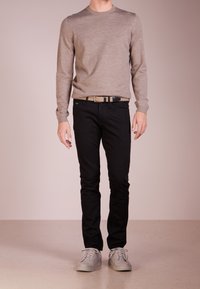 Jasnobrązowy sweter z długim rękawem, czarne slim-fit dżinsy i szare sneakersy. Prosty design, ściągacze na rękawach i teksturowany materiał w swetrze.