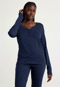 Navy blue loungewear set featuring long sleeves, a V-neckline, and white dot pattern. Fabric appears soft with a relaxed fit.