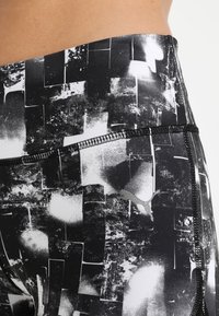 Černobílé tištěné sportovní legíny s geometrickými vzory, s vysokým pasem a viditelnými švy, vyrobené z elastického materiálu.