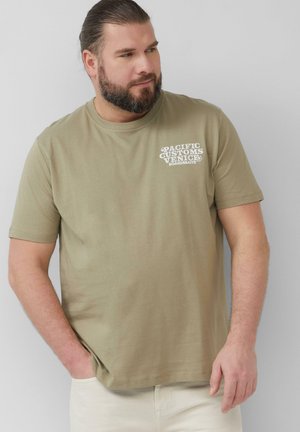 Olijfgroene katoenen t-shirt met korte mouwen, ronde halslijn en witte tekstprint aan de linkerzijde. Glad textuur en casual pasvorm.