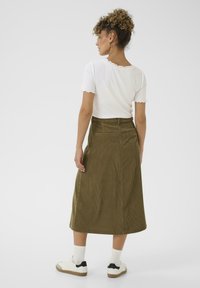 Olive green corduroy midi skirt with a fitted waist, pockets, and vertical stripes. Paired with a white ribbed short-sleeve top and sneakers.