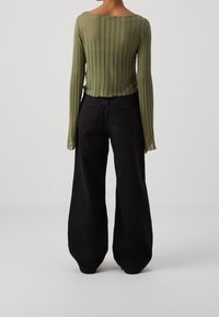 Grünes, geripptes Langarmoberteil mit weitem Rundhalsausschnitt, kombiniert mit schwarzen, weit geschnittenen Jeans mit Gesäßtaschen und glatter Textur.