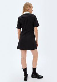 Vestido negro de manga corta con cuello blanco, diseño ajustado y falda ligeramente acampanada. Tejido texturizado con un aspecto limpio y bien elaborado.