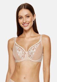 Nude bezprzewodowy stanik z przezroczystymi koronkowymi miseczkami w kwiatowy wzór, z miękkim podszyciem i delikatnym białym wykończeniem na brzegach i ramiączkach.