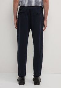 Marineblaue Hosen aus einem weichen Material, mit einer lockeren Passform, elastischem Bund und zwei Gesäßtaschen. Aufgerollte Säume und minimalistisches Design.