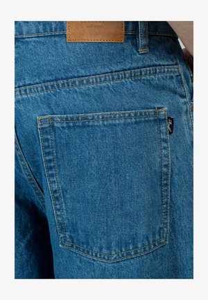 Die Denim-Jeans haben eine blaue Farbe mit einer leicht verblassten Textur, einer hinteren Tasche und einem Lederpatch mit eingeprägtem Branding am Bund.