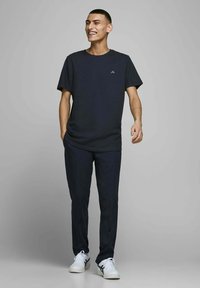 Mørkeblå crew neck T-shirt med logo, parret med mørke bukser og hvide sneaker. Outfitten har en afslappet pasform og en glat tekstur.