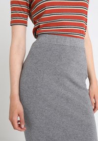 Šedá žebrovaná pletená tužková sukně s vysokým pasem, kombinovaná s červeno-bílým proužkovaným tričkem s krátkým rukávem. Hladká textura, přiléhavý střih.