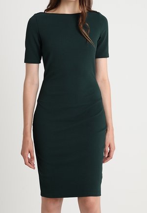 Donker groene nauwsluitende jurk tot op de knie met korte mouwen, ronde hals, gestructureerde stof en subtiele plooien bij de taille.