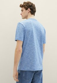 Modra heather bombažna majica s krojem in kratkimi rokavi, ki prikazuje sproščen kroj in gladko teksturo, kombinirana z jeans hlačami.