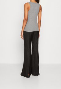 Szary top bez rękawów o dopasowanym kroju zestawiony z czarnymi, szerokimi spodniami z bocznymi rozcięciami, oba wykonane z lekkich tkanin.