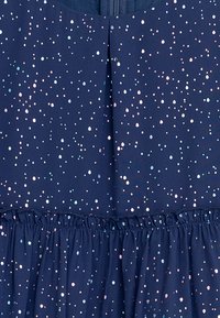 Navy-Kleid aus Stoff mit geraffter Taille, verziert mit gepunkteten pastellfarbenen Dots. Das Design umfasst einen Rückenreißverschluss und einen fließenden Saum.