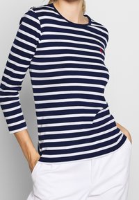 Granatowa i biała striped bluzka z długim rękawem, okrągłym dekoltem i małym czerwonym logo. Miękka tkanina i luźny krój.