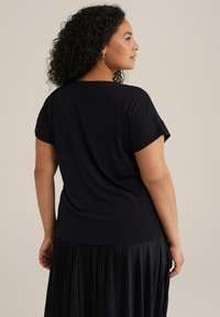 Top corto nero a maniche corte realizzato in tessuto morbido con vestibilità rilassata, abbinato a una gonna nera plissettata, visto da dietro.