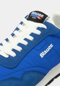 Μπλε αθλητικά παπούτσια με λευκά κορδόνια και σήμανση. Κατασκευασμένα από υφασμάτινο υλικό με υφή, διαθέτουν καμπυλωτό σχεδιασμό και μαύρη γλώσσα με λογότυπο.