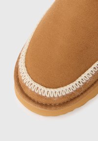 Brune suede sko med rund form, med en hvit søm rundt kanten og en gummisåle for godt feste.