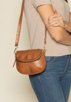 Braune Leder-Crossbody-Tasche mit geschwungenem Design, Reißverschlussverschluss und goldenen Hardware-Akzenten. Verstellbarer Gurt für vielseitigen Tragekomfort.