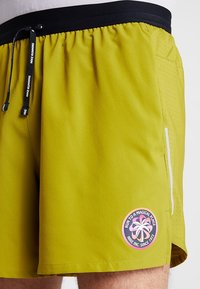 Nike-Laufshorts aus einem leuchtend gelb-grünen Stoff. Sie verfügen über einen schwarzen elastischen Bund, eine Seitentasche mit weißem Reißverschluss und ein Logo-Emblem.