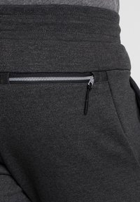 Mörkgrå träningsbyxor med en dragkedjeficka med svart kant, tillverkade av textil med strukturerad yta och sl ät finish.