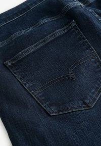 Țesătura de denim de culoare albastru închis prezintă o căptușeală pe spate cu detalii subtile de cusătură și un finisaj texturat. Țesătura pare moale și durabilă.