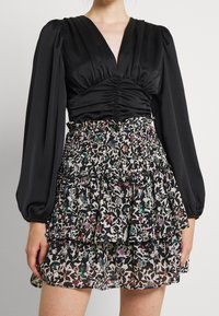 Top de satén negro con mangas abullonadas, combinado con una falda de varios niveles estampada con flores en negro, blanco y acentos de color.