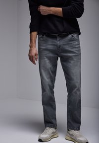 Jeans de mezclilla gris con un corte regular, tiro medio y un acabado ligeramente deslavado. Combinados con zapatillas de color claro.