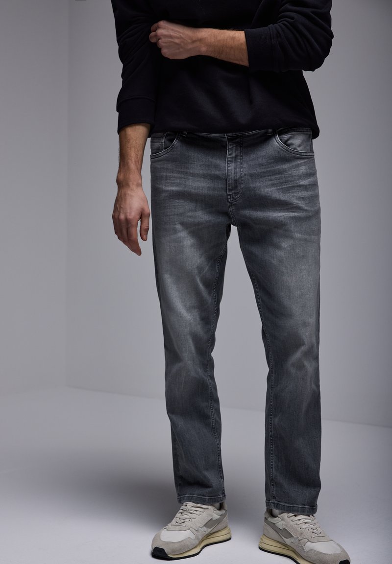 Jeans de mezclilla gris con un corte regular, tiro medio y un acabado ligeramente deslavado. Combinados con zapatillas de color claro.