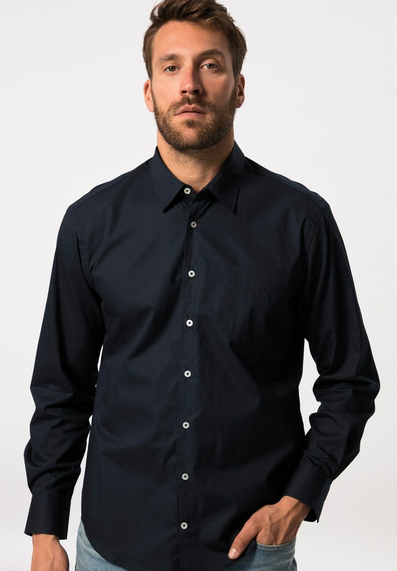 Merkkipaitana on puuvillainen tummansininen napitettava paita, jossa on pitkät hihat, etutasku ja valkoiset napit. Tekstuuriltaan sileä ja leikkaukseltaan istuva.