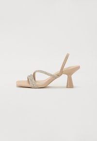Sandali con tacco alto beige, con punta quadrata, dotati di due cinturini incrociati in strass e un tacco geometrico e trasparente.