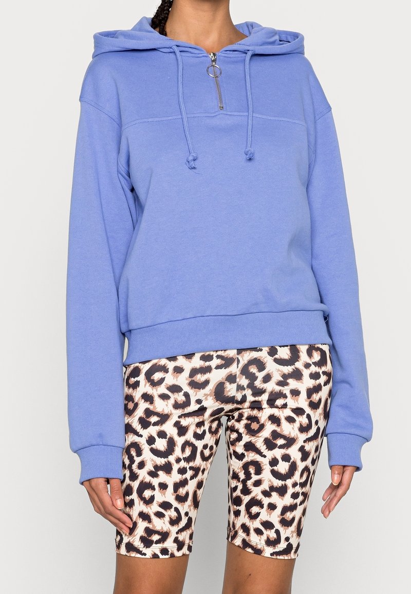 Ljusblå huvtröja med dragkedja fram, långa ärmar och ribbad fåll. Matchas med mönstrade cykelbyxor i knälängd med leopardtryck.