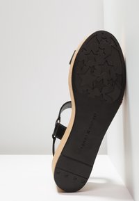 Semelle noire de sandale avec motif d'empreinte en forme d'étoile et marquage "Tommy Hilfiger" sur talon compensé beige clair.