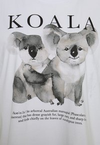 Bílý tričko s ilustrací dvou koal s šedým kožichem a velkýma ušima, doplněné textem popisujícím druh a habitat.