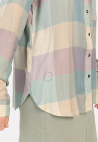 Long-sleeve button-up shirt in pastel shades of blue, mint, and pink with a herringbone pattern and a curved hem. Features logo detail.