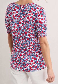 Blusa floral con un fondo blanco, flores rojas y hojas azules, mangas abullonadas con elástico y escote redondeado.
