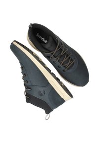 Blauwe synthetische sneakers met een gladde textuur, witte rubberen zool en bruine veters. Beschikt over een gevoerde kraag en een logo aan de zijkant.