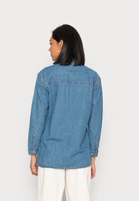 Denimskjorte, lys blå, lange ermer, knappede mansjetter, ryggdetalj, avslappet passform, rett kant, myk tekstur.