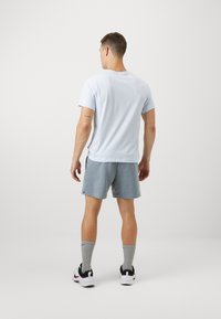 Cămășă din bumbac de culoare albastru deschis, pantaloni scurți atletici gri, adidași albi cu accente negre și șosete gri. Design simplu, fără modele.