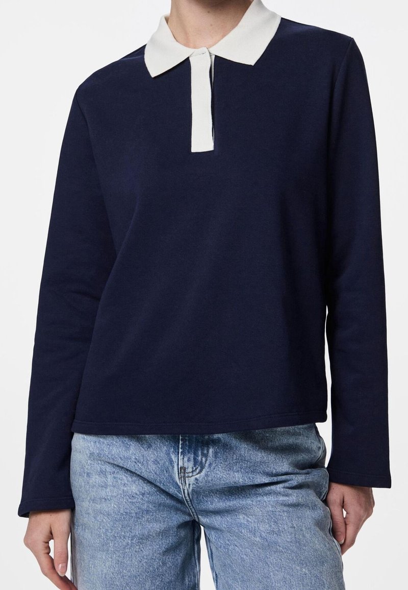 Polo à manches longues bleu marine avec un col blanc. Matière en coton, coupe décontractée et design simple. Assorti à un jean denim bleu clair.