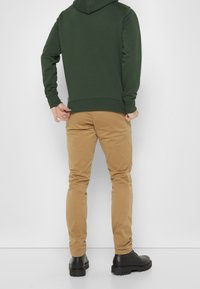 Green hoodie with a relaxed fit, beige pants with a slim profile, and black lace-up boots on a plain background.
