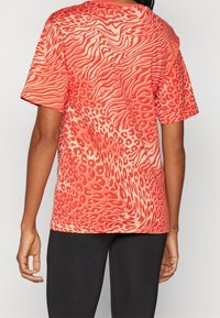 Lyhythihainen punainen t-paita, jossa on pyörteilevä, aaltoileva kuvio ja leopardin täpliä. Valmistettu kevyestä kankaasta, rento istuvuus ja pyöreä pääntie.