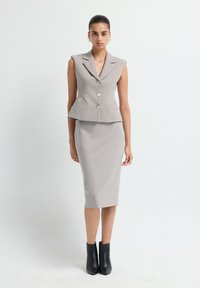 Grau gefütterte ärmellose Blazerjacke mit zwei Knöpfen und passendem Bleistiftrock, ergänzt durch schwarze Ankle-Boots aus glattem Material.