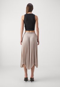 Top corto negro de tirantes con un diseño ajustado, combinado con una falda larga beige con pliegues. La falda presenta una cinturilla suave y una textura fluida.